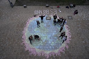 Schüler*innen des Mediencampus Babelsberg haben mit Kreide eine brennende Erde auf den Schulhof gemalt