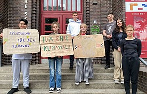 Schüler*innen der Ida Ehre Schule halten selbst gemachte Klimaschutz-Plakate in die Kamera