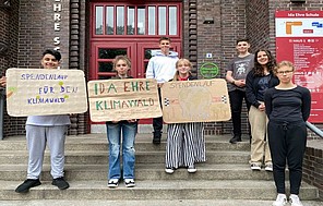 Schüler*innen der Ida Ehre Schule halten selbst gemachte Klimaschutz-Plakate in die Kamera