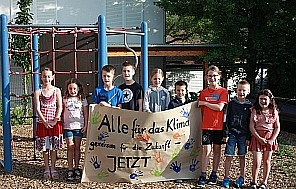 Die Schüler*innen der Grundschule am Jakobsweg stehen mit selbst gestaltetem Klimaschutz-Plakat vor dem Klettergerüst