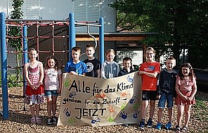 Die Schüler*innen der Grundschule am Jakobsweg stehen mit selbst gestaltetem Klimaschutz-Plakat vor dem Klettergerüst